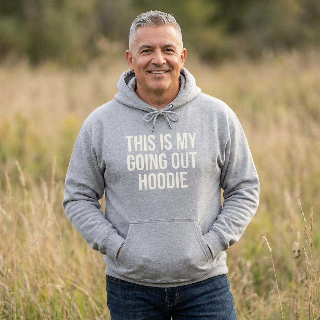 Man wearing a gray hoodie with text standing in a field